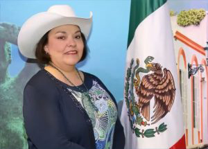 Embajadora mexicana posado a un lado de bandera de México